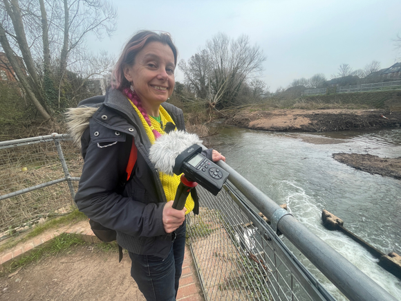 Bel Deering at Firepool Weir. Bel is holding a sound recorder and smiling at the camera