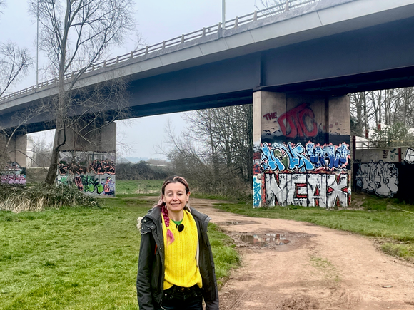 Bel Deering in a bright yellow top standing by a graffiti covered underpass in Taunton